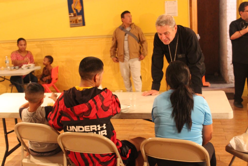 A family from the asylee community are seated at a table talking to Bishop Brennan.