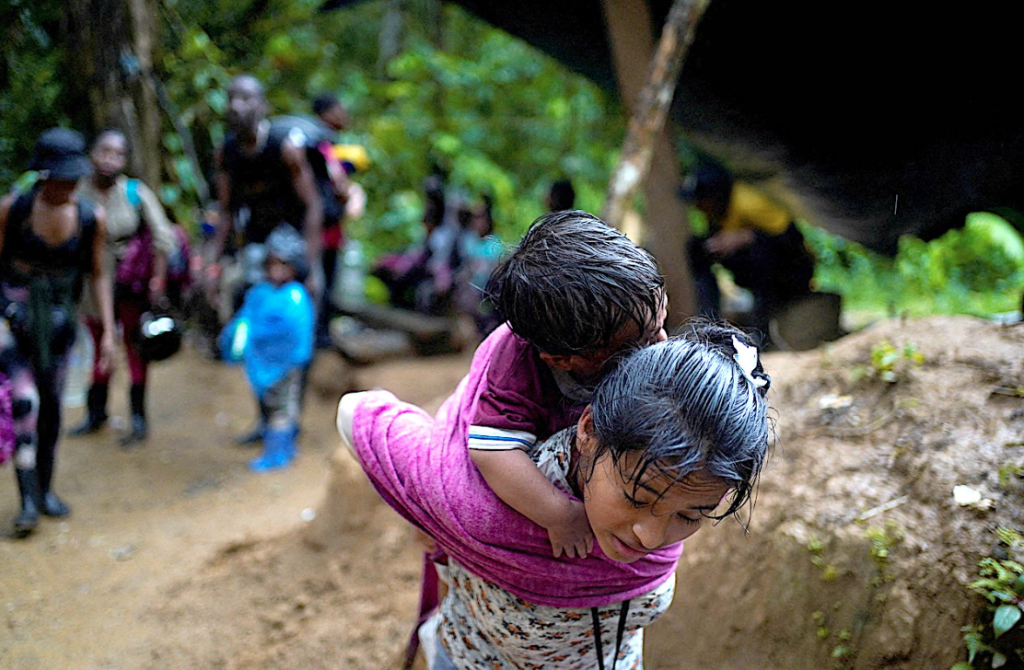 A young migrant woman carries a child on her back as she enters the Darien Gap. Others migrants are behind her.