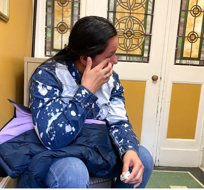 A migrant mother is seated wiping her tears.