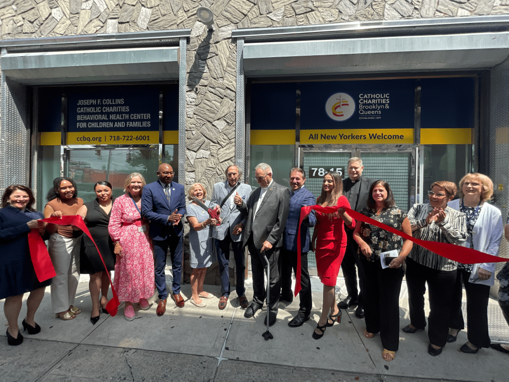 Group of people cutting red ribbon with large scissors in front of building.